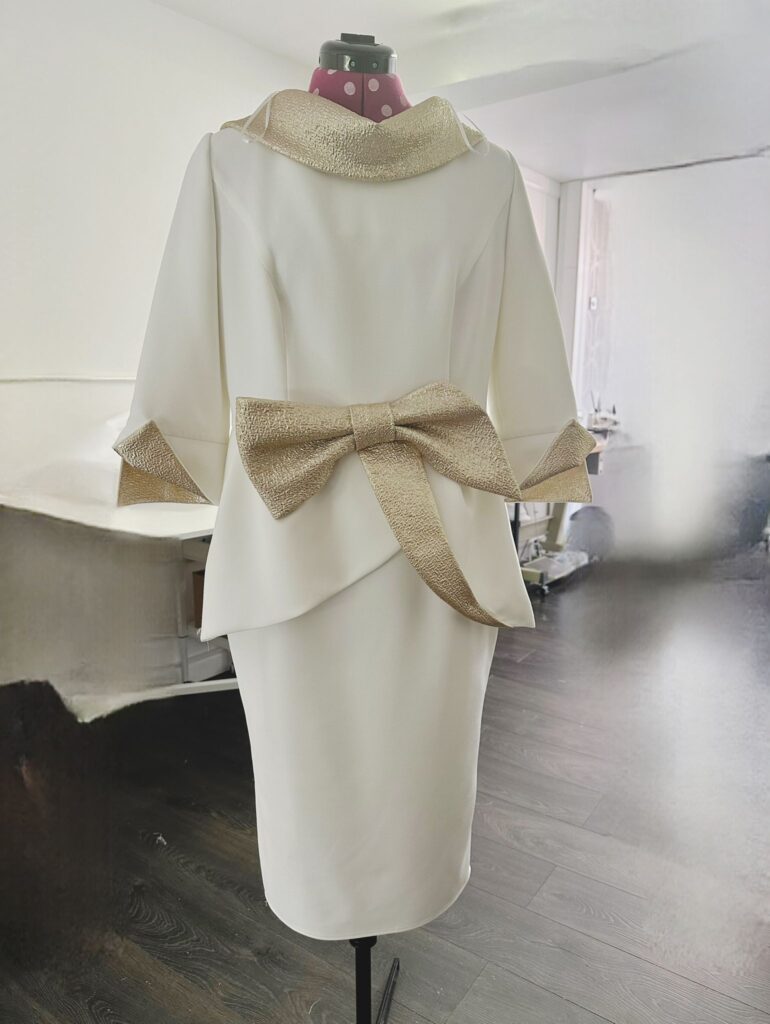 Close-up of a tailored cream dress with a decorative gold bow.